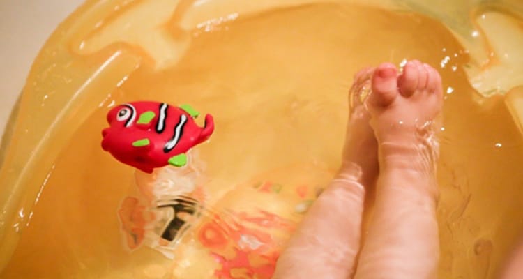 baby's feet in a bath tub with a floating fish toy
